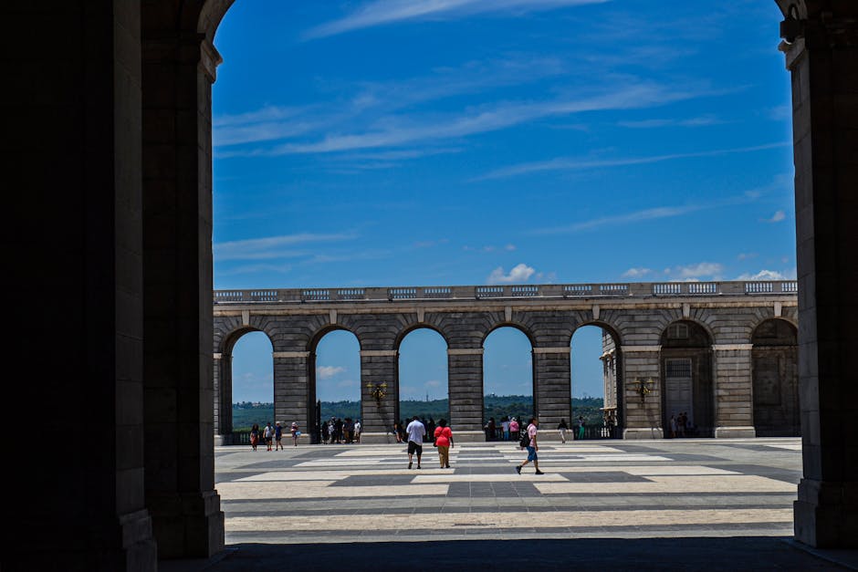 View of the Royal Palace courtyard in Madrid with people walking under a clear blue sky.